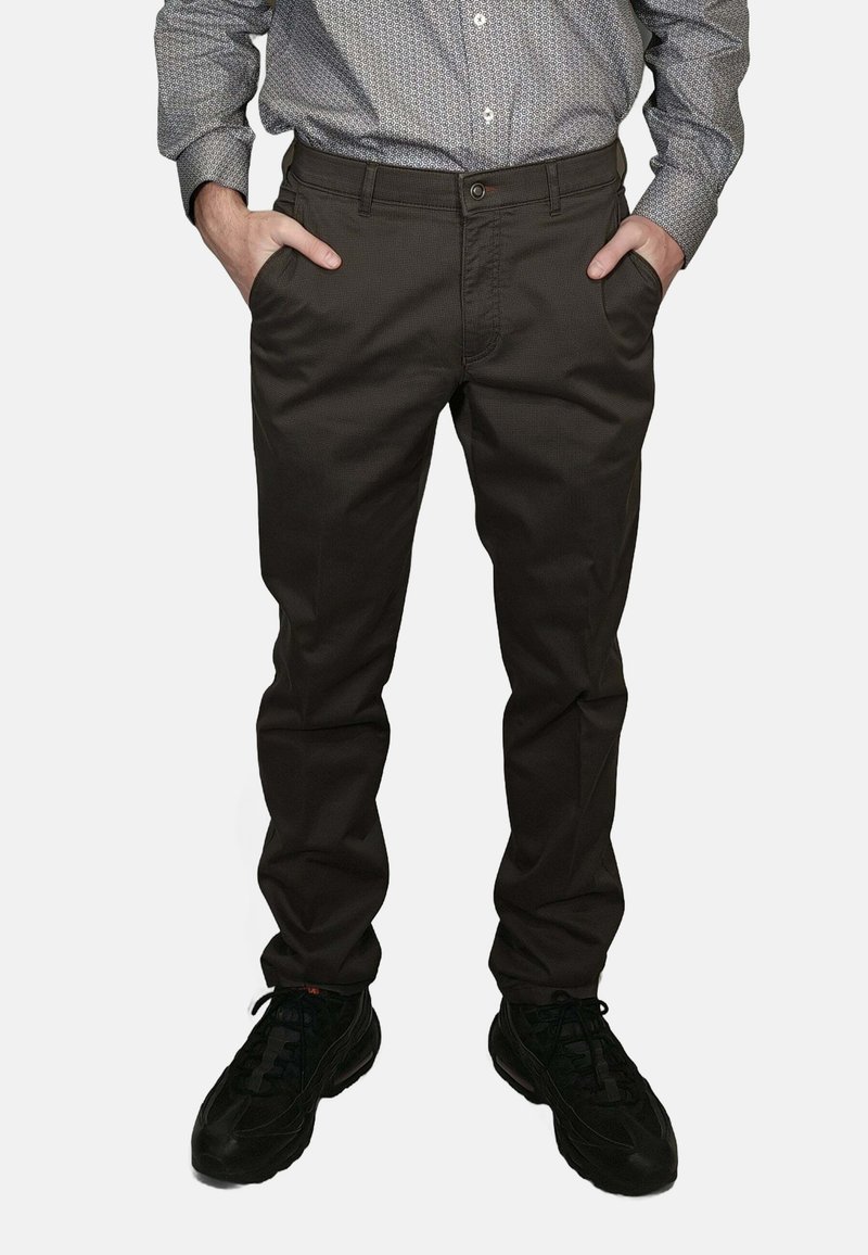 Pantaloni marrone scuro dal taglio slim, con fronte piatto, tasche laterali e passanti per cintura, abbinati a sneakers nere e una camicia a fantasia.