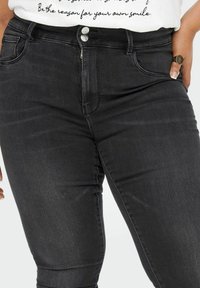 Zwarte skinny jeans met een gladde denimtextuur, voorzien van een rits en twee voorzakken. De tailleband heeft riemlussen voor extra stijl.