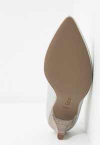Chaussure à talon haut argentée à bout pointu, affichée semelle vers le haut, taille 4½, avec une semelle extérieure beige texturée et un talon empilé mince.