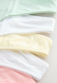 Pile de masques faciaux en coton de couleur pastel avec bords festonnés sur un fond clair.