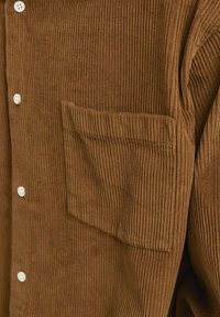 Chemise boutonnée en velours côtelé marron avec une texture à côtes verticales, boutons blancs et une poche poitrine unique pour une touche de détail.