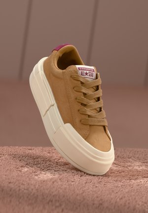 Sneaker in suede beige con suola in gomma crema, caratterizzata da punta arrotondata, lacci piatti e linguetta sul tallone color bordeaux con il logo Converse.