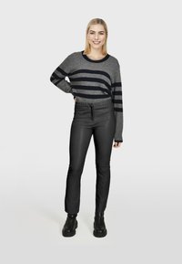 Sivi i mornarski prugasti pulover, opuštenog kroja, u kombinaciji s crnim hlačama na elastiku. Model nosi debele crne čizme. Neutralna pozadina.