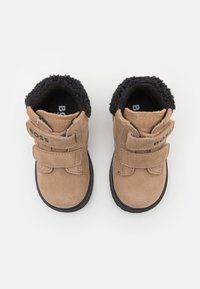 Brune semskede ankelstøvler med to borrelåsremmer, en krave med sort pelsfoder og en gummisål med struktureret greb.