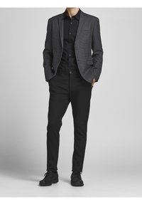 Grå texturerad blazer med svart knäppskjorta, svarta byxor och svarta finskor. Blazern har en enkel ficka och en strukturerad passform.