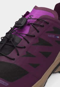 Κοντινή λήψη μωβ και μαύρου παπουτσιού πεζοπορίας με σύστημα γρήγορου δέσιμου, τριγωνικά μοτίβα από δίχτυ και λογότυπα "MATRIX" και "GORE-TEX" στο πλάι.