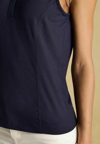 Marineblaues ärmelloses Oberteil mit weicher Textur, rundem Ausschnitt und vertikalen Nähten, kombiniert mit weißen Hosen am unteren Rand.