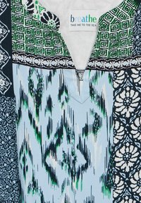 Tela de patrón multicolor con azules, verdes y negro. Presenta diseños geométricos, un patrón ikat y acentos florales. Detalle en forma de V.