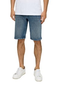 Shorts en denim bleu clair, longueur mi-cuisse, avec un délavage et des ourlets roulés, associés à des baskets blanches.