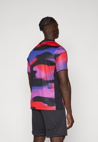 Short-sleeve athletic shirt in a vibrant abstract pattern of red, purple, and blue, with black side panels; made of lightweight, stretchy fabric.