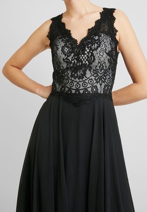 Robe noire avec corsage en dentelle à motifs floraux, encolure en V, superposition transparente, jupe fluide, design sans manches.