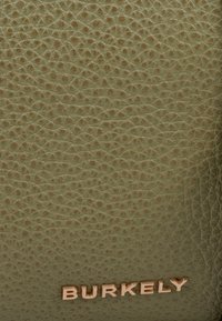 Pelle in verde oliva con texture e piccole protuberanze, con un logo "BURKELY" in tonalità oro nella parte inferiore. Finitura liscia con un aspetto opaco.