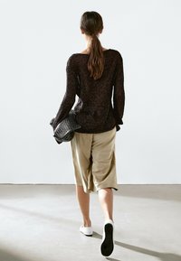 Černý pletený top s dlouhým rukávem, béžové široké šortky a bílé boty na slip. Model ukázán zezadu na světlém pozadí.