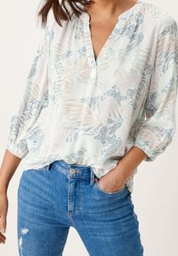 Blouse légère à motif avec encolure en V, manches fluides, et une palette de couleurs pastel mint, rose et bleu, associée à un jean en denim.