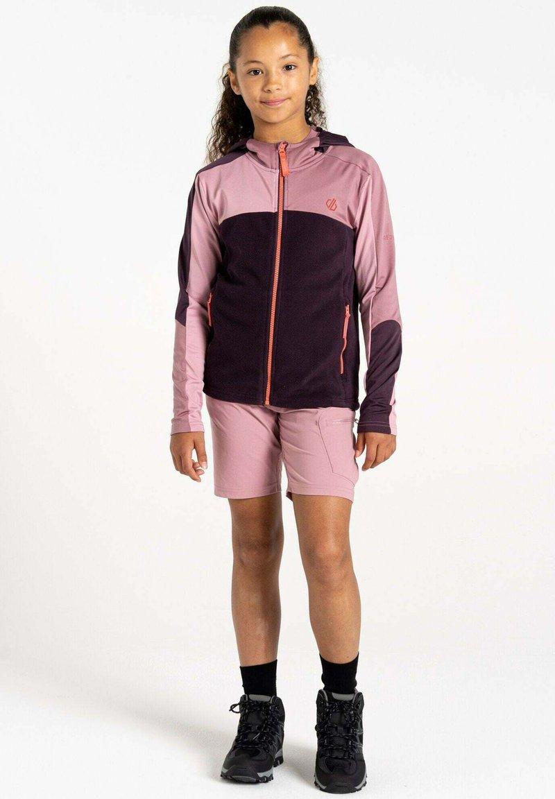 Fleece-Jacke mit Reißverschluss in Pink und Dunkelviolett, kombiniert mit pinken Shorts. Verfügt über eine Kapuze und einen kontrastierenden orangen Reißverschluss, getragen mit schwarzen Wanderschuhen.