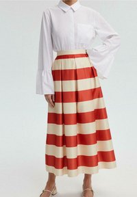 Chemise blanche à col avec manches évasées associée à une jupe plissée beige à rayures rouges, présentant un design complet et fluide.