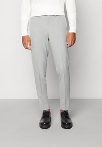 Szare spersonalizowane spodnie wykonane z lekkiego materiału o gładkiej fakturze. Charakteryzują się slim fit i płaskim przodem, zestawione z czarnymi sznurowanymi butami.