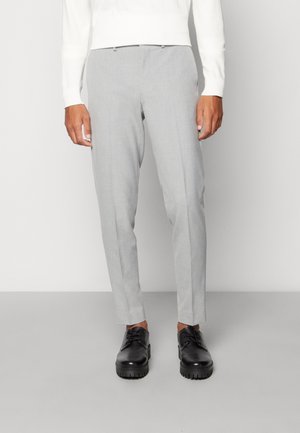 Pantaloni grigi su misura realizzati in un tessuto leggero con una texture liscia. Presentano una vestibilità slim e una parte anteriore piatta, abbinati a scarpe nere con lacci.
