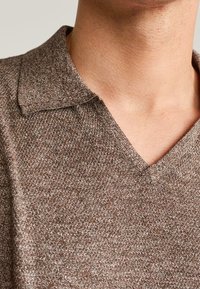 Hnědá pletená polo košile s texturou, výstřihem do V a krátkým límcem. Měkká tkanina s jemným vzorem, vhodná pro každodenní nošení.
