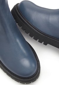 Leder-Ankle-Boots in Dunkelblau. Runde Zehenform, strukturierte Oberfläche, dicke schwarze Sohle mit Profil. Minimalistisches Design und klare Linien.