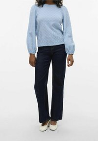Light blue textured long-sleeve top with puffed sleeves paired with dark blue straight-leg jeans and white flat shoes.
