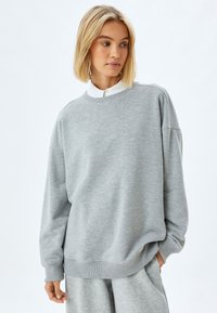 Grauer Pullover mit Rundhalsausschnitt, langen Ärmeln und gerippten Bündchen. Weicher Stoff mit lockerer Passform und minimaler Nahtgestaltung.