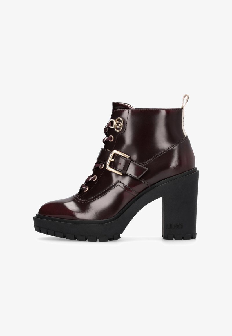 Bottine brillante bordeaux foncé à la cheville avec talon haut épais, semelle épaisse à crampons, fermeture à lacets à l'avant et sanglette décorative avec boucle latérale.