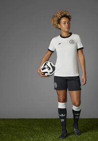 White ribbed jersey with black accents, black shorts, and knee-high socks. The individual holds a black-and-white soccer ball.