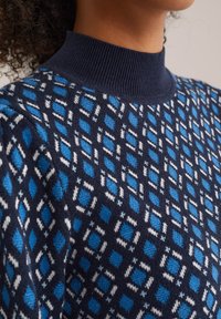 Maglione lavorato a maglia con una base blu navy e un motivo geometrico in diverse tonalità di blu e bianco. Collare alto a coste.