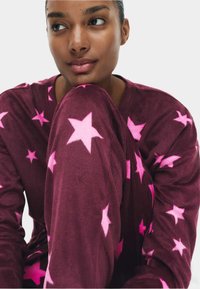 Conjunto de ropa de estar en burdeos de forro polar con grandes patrones de estrellas rosas, mangas largas y un ajuste relajado, que ofrece una textura suave y acogedora.