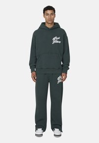 Donkergroene hoodie en bijpassende sweatpants, beide gemaakt van katoen, met een wit "Good for Nothing" logo op de borst en bovenbeen.