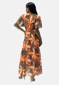 Robe maxi orange avec un motif floral feuillu. Présente des manches courtes à volants et une taille froncée. Tissu léger et fluide, longueur cheville.