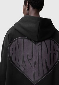 Felpa con cappuccio nera caratterizzata da una grande grafica a forma di cuore di colore viola scuro con testo stilizzato in un contorno nero a contrasto.