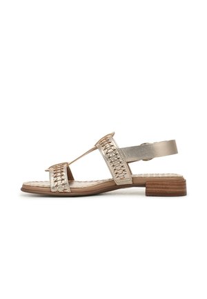 Flat sandal in metallic gold leather with woven detail, open toe design, and adjustable ankle strap. Features a low wooden heel.