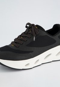 Basket noir de sport avec tige en maille, surface texturée, col rembourré et semelle épaisse blanche dotée d'outils pour la flexibilité et le soutien.