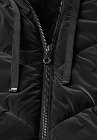 Giubbotto nero imbottito con design a zigzag, caratterizzato da una cerniera argentata, cordini neri regolabili e una texture liscia e lucida.
