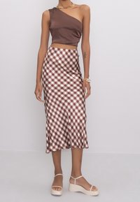 Ruskea yksolkaiminen lyhyt toppi yhdistettynä ruskeaan ja valkoiseen ruudulliseen midi-hameeseen. Malli käyttää korokepohjasandaaleja nilkkaremmeillä.