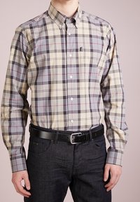 Knoopshirt van katoen in beige met een grijs en donkerrood ruitpatroon; heeft een kraag en knopenmanchetten, gecombineerd met donkere spijkerbroeken en een zwarte riem.