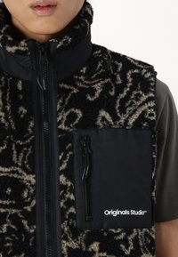 Black and cream patterned fleece vest with high collar, front zipper closure, and side pocket featuring black fabric and logo.