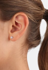 Silberner, sternförmiger Ohrring mit polierter Oberfläche, im durchstochenen Ohr getragen, der klare Linien und ein minimalistisches Design präsentiert.