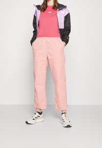 Vrstvený outfit s černou a levandulovou větrovkou, růžovým tričkem a svetelně růžovými volnými kalhotami, doplněný bílými sportovními botami.