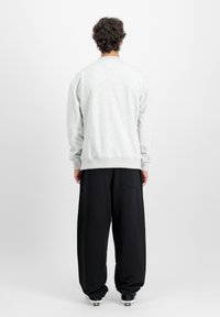 Siv sweatshirt z dolgimi rokavi, rebrastimi manšetami in robom, v kombinaciji s sproščenimi črnimi hlačami. Sproščen in udoben dizajn.