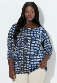 Marineblå langærmet top med geometrisk print i forskellige nuancer af blå og creme; blødt stof med rund halsudskæring og buet kant.