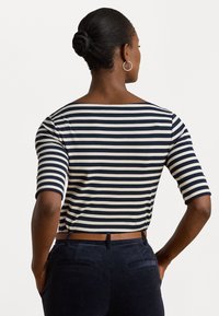 Tumesinine ja koorevalge triibuline topp, millel on paadikaela lõige ja kolmveerandvarrukad, koos tumedate pükste ja pruuni vöödiga. Sile kangatekstuur.