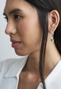 Cercei din argint în formă de stele, cu o piatră verde prețioasă. Designul combină elemente texturate și netede, evidențiind finisaje contrastante.