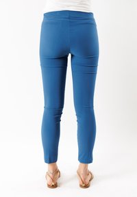 Pantaloni elastici blu con una texture liscia, vita alta e design aderente che si restringe alle caviglie, abbinati a sandali color sabbia.