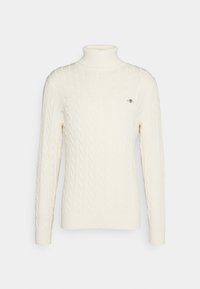 Crème kabelbrei coltrui in een zachte textuur met ribgebreide manchetten en zoom, met een klein logo op de borst.
