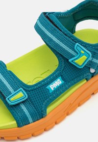 Teal netting sandal med lyseblå striper og gule detaljer. Har justerbare stropper og en oransje gummisåle. PMG-logo synlig.