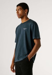 Tamnoplava pamučna majica kratkih rukava s okruglim izrezom i ležernim krojem. Na prsima ima diskretan otisak logotipa.