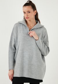 Pulover oversized gri, cu guler înalt, fermoar pe jumătate, detalii nervurate pe guler și țesătură tricotată texturată. Croială casual.